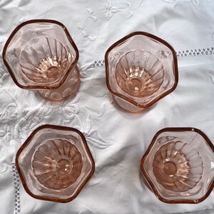 May include: Four pink glass dessert cups with a fluted design. The cups are arranged in a square pattern on a white tablecloth.