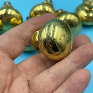 May include: A close-up of a gold-toned cabinet knob with a round, slightly domed shape. The knob is smooth and shiny, with a slight sheen.