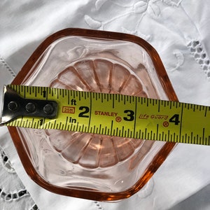 May include: A pink glass dish with a scalloped edge, measuring approximately 3 inches in diameter. The dish is sitting on a white fabric surface.