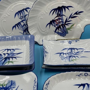 May include: Set of white ceramic plates with blue and green bamboo designs. The plates are in various shapes and sizes, including square, oval, and round.