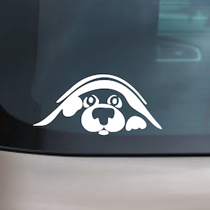 Puede incluir: Pegatina de coche de vinilo blanco de un perro de dibujos animados asomándose por la ventana de un coche. El perro tiene la cara blanca con ojos negros y la nariz negra.