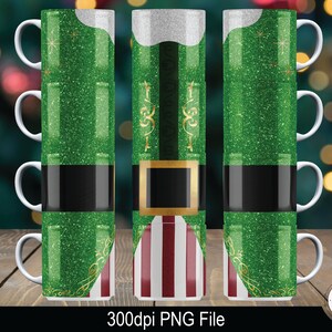 May include: Three white mugs with a green, black, and gold glitter design of an elf costume. The design includes a green hat, black belt, and red and white striped pants. The mugs are stacked on top of each other.