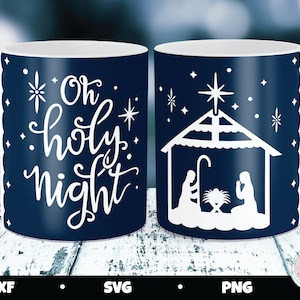 May include: Two white ceramic mugs with blue interiors. One mug features the text "Oh holy night" in white script with stars. The other mug features a white silhouette of the nativity scene with a star above the manger.