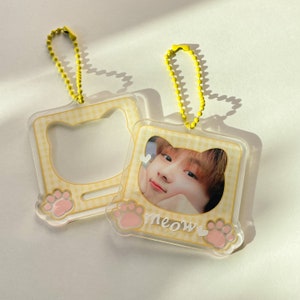 May include: Two clear plastic keychain frames with yellow chains. One frame has a paw print and the word "meow" with a heart. The other frame has a paw print and a blank space for a photo.