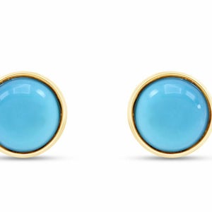 Puede incluir: Un par de pendientes de botón redondos. Cada pendiente presenta una piedra turquesa brillante engastada en un bisel dorado. Los pendientes se muestran sobre un fondo blanco.