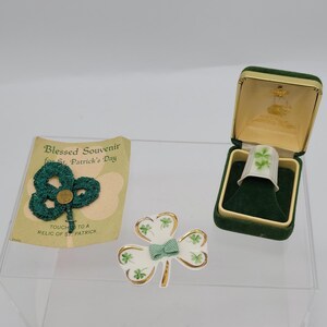 Könnte beinhalten: Eine grüne Kleeblatt-Anstecknadel, ein weißer Fingerhut mit einem grünen Kleeblatt-Design in einer grünen Samtbox und eine Karte mit der Aufschrift "Gesegneter Souvenir zum St. Patrick's Day. Berühren Sie ein Relikt des Heiligen Patrick."