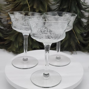 Könnte beinhalten: Satz von vier klaren Weingläsern mit Stiel aus Glas mit einem geätzten Design. Die Gläser sind auf einer weißen runden Oberfläche angeordnet.
