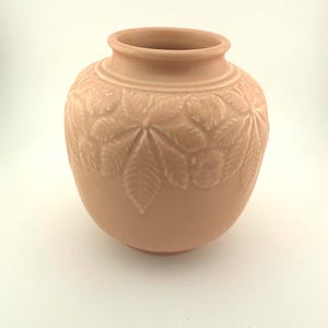 May include: A set of three ceramic mugs with a speckled, cream-colored glaze. Each mug features a different hand-painted design: a blue and green leaf, a yellow flower, and a red berry. The mugs have a simple, rounded shape.