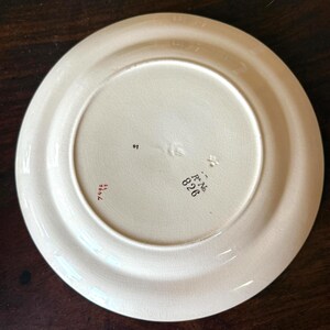 May include: Off-white ceramic plate with a wide rim. The underside features stamped text including "R No. 826" and "7496". The plate has a slightly aged appearance, suggesting it is vintage or antique.