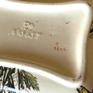 May include: Cream-colored ceramic serving dish with a floral design featuring yellow daisies and green leaves. The dish has a wavy shape and is marked with the numbers "18627" and "964".