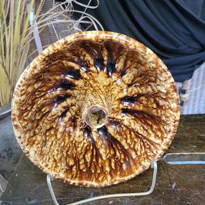 Pode incluir: Uma forma de bolo bundt de cerâmica envidraçada marrom e amarela com um furo central. A forma está em um suporte de metal dourado.