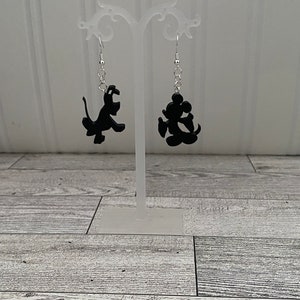 May include: A pair of dangle earrings featuring black silhouette charms of Mickey Mouse and Pluto. The earrings are hanging from silver hooks.