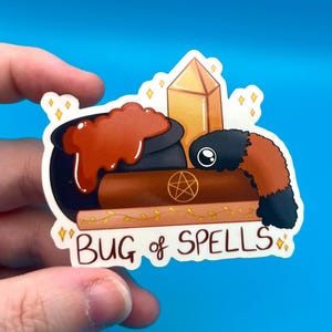May include: A sticker featuring a cartoon bug with a cauldron, a crystal, and a book. The text "Bug of Spells" is written on the sticker.