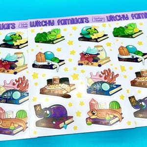 Könnte beinhalten: Ein Set mit 12 Hexen-Familien-Stickern mit verschiedenen Kreaturen und magischen Gegenständen. Jeder Sticker ist auf weißem Hintergrund mit gelben Sternen und zeigt ein Buch mit einer anderen Kreatur oder einem anderen Gegenstand darauf. Die Sticker beinhalten einen Frosch, einen Kristall, ein Meereswesen, einen Drachen und mehr.