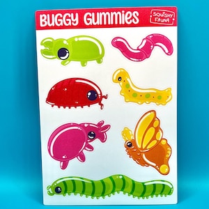 Op de afbeelding: Een vel met kleurrijke, cartoonachtige stickers met verschillende insecten, waaronder een groene kever, een rode lieveheersbeestje, een roze slak, een gele vlinder, een gele worm en een groene worm. De stickers zijn gelabeld met "Buggy Gummies" en "Squishy Fauna".