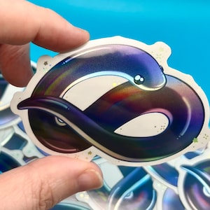 Puede incluir: Una pegatina holográfica de una anguila púrpura iridiscente enroscada con un fondo blanco y detalles de purpurina dorada.