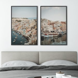 May include: Two framed photographs of a colorful town on a hillside overlooking a harbor with boats. The town is built on a steep cliff with many buildings and houses. The water is a deep blue and the sky is a light blue.