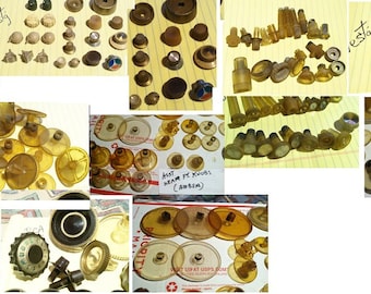 May include: A collection of vintage amber-colored radio knobs and components, including various sizes and shapes. Some knobs have white or black accents. The image also includes the handwritten word "West" and "restg".