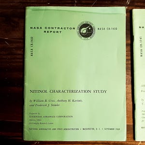 May include: A light green NASA Contractor Report titled "Nitinol Characterization Study." The report, NASA CR-1433, includes the NASA logo and was prepared by Goodyear Aerospace Corporation in September 1969.