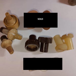 May include: Assortment of vintage plastic knobs and caps in brown, beige, and white. The knobs have a ridged design and the caps have a variety of shapes. The text "SOLD" is visible in the image.
