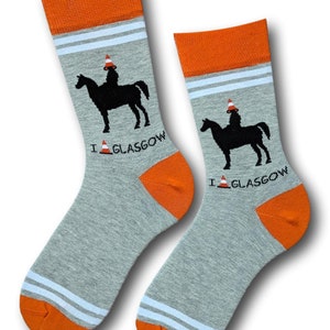 May include: A pair of gray socks with orange and white stripes. The socks feature a black silhouette of a person riding a horse wearing a traffic cone on their head. The text "I  GLASGOW" is printed on the socks with a traffic cone icon.