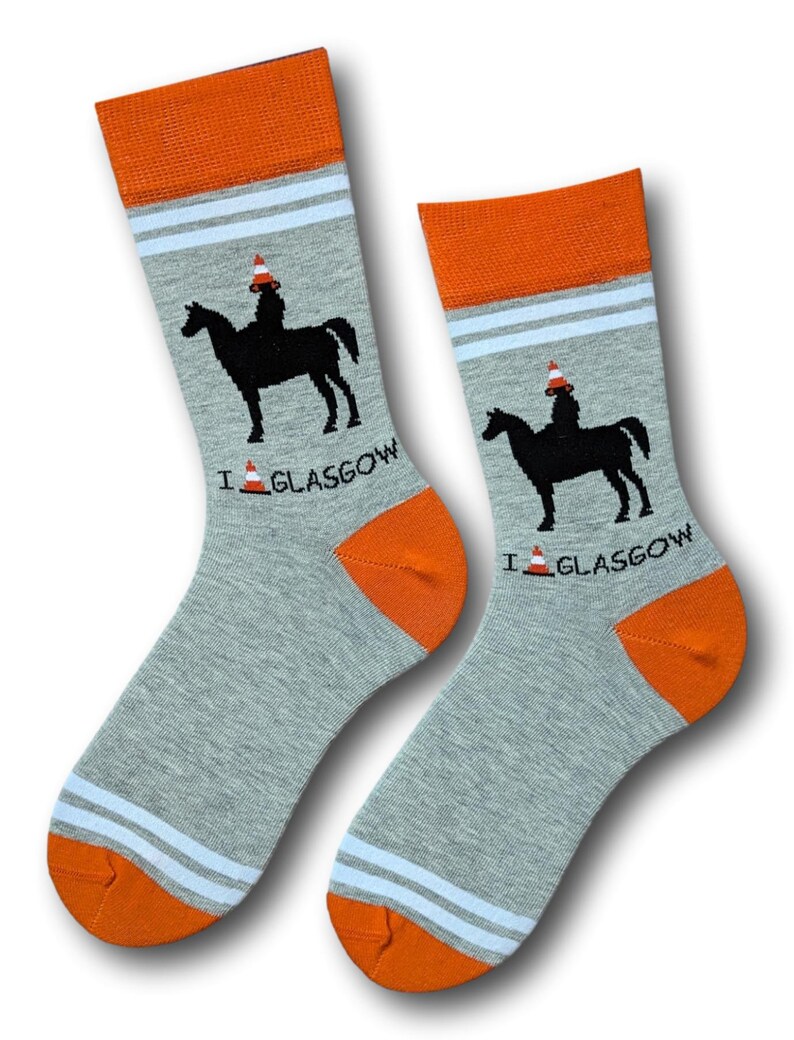 May include: A pair of gray socks with orange and white stripes. The socks feature a black silhouette of a person riding a horse wearing a traffic cone on their head. The text "I  GLASGOW" is printed on the socks with a traffic cone icon.