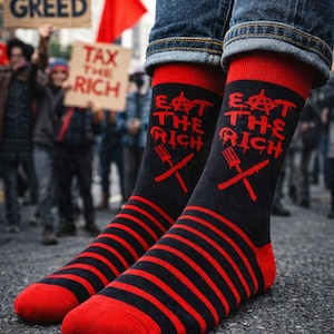 May include: Black and red striped socks with the slogan "EAT THE RICH" and a fork and knife design. The socks are worn with blue jeans. The background shows a protest with signs and a red flag.