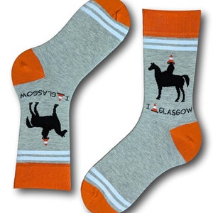 May include: A pair of gray socks with orange and white stripes. One sock has a black silhouette of a horse wearing a traffic cone on its head. The other sock has a black silhouette of a horse lying down with a traffic cone on its head. Both socks have the text "I  GLASGOW" on them.