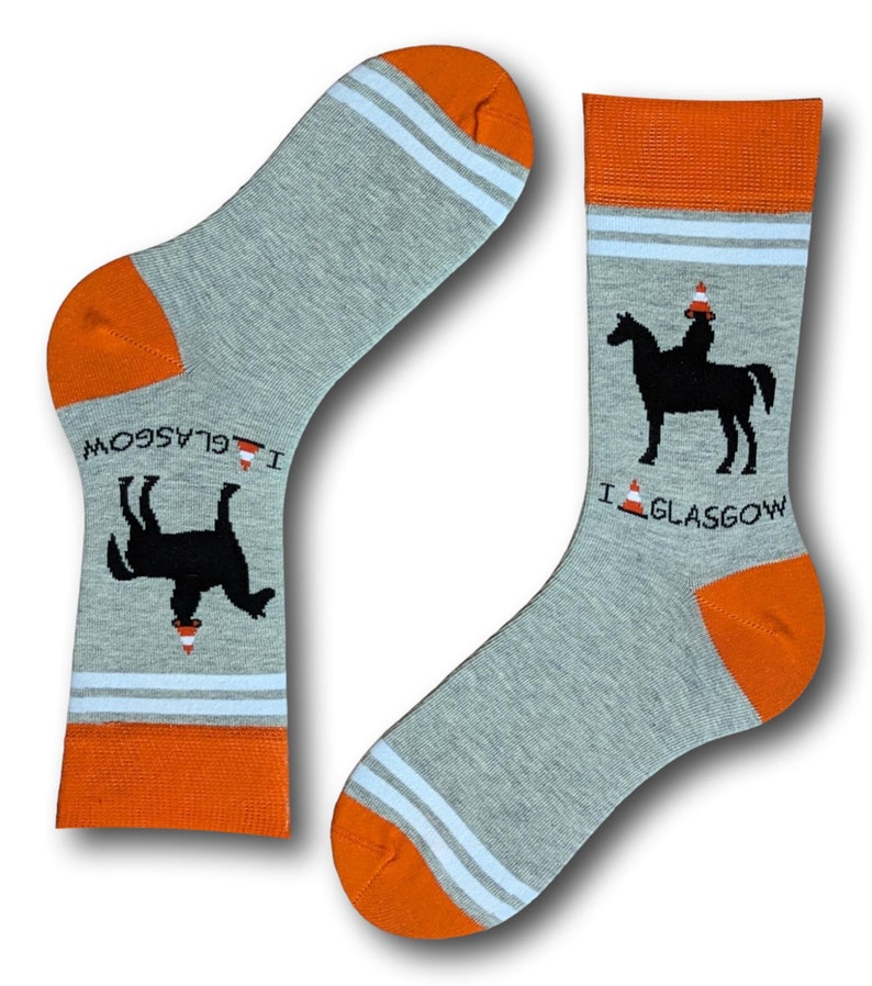 May include: A pair of gray socks with orange and white stripes. One sock has a black silhouette of a horse wearing a traffic cone on its head. The other sock has a black silhouette of a horse lying down with a traffic cone on its head. Both socks have the text "I  GLASGOW" on them.