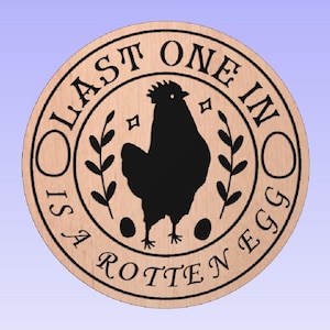Pode incluir: Placa redonda de madeira com uma silhueta de galo preto, o texto "LAST ONE IN IS A ROTTEN EGG" e elementos decorativos. A placa é castanho-claro com borda e texto pretos.