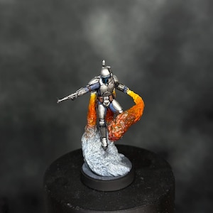 Puede incluir: Figura en miniatura detallada de un personaje con armadura plateada y azul, sosteniendo un bláster. La figura está en el aire, con llamas naranjas y amarillas que emanan de su espalda, montada sobre una base gris.