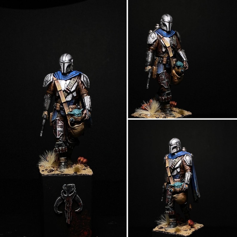 May include: A silver and blue action figure of a Mandalorian warrior holding a small green figure. The Mandalorian is wearing a helmet and armor, and is holding a blaster rifle in one hand. The figure is standing on a base with a brown and green background.