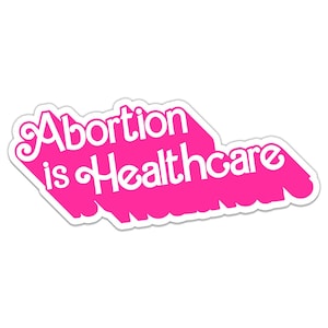 Pode incluir: Etiqueta rosa com texto branco que diz "Aborto é saúde".