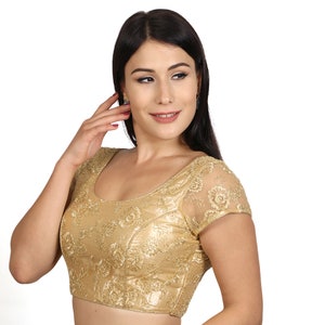 May include: A gold embroidered blouse with short sleeves and a scoop neckline. The blouse is made of a sheer fabric with a floral pattern.