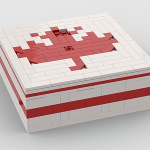 Könnte beinhalten: Eine weiße Box mit einem roten Ahornblatt-Design auf der Oberseite und roten Streifen an den Seiten. Die Box ist aus Lego-Steinen gefertigt.