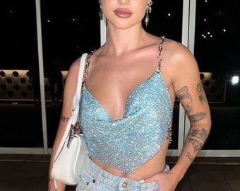 Peut inclure: Une femme portant un haut court scintillant bleu clair avec une bretelle en chaîne argentée, un jean denim bleu clair et des talons scintillants bleu clair.