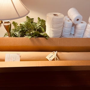 Puede incluir: Una caja de cart&oacute;n llena de suministros para manualidades. En el interior hay varias bobinas de cord&oacute;n de algod&oacute;n blanco, rollos de papel envuelto y una tarjeta peque&ntilde;a. Se ven plantas verdes con forma de helecho.