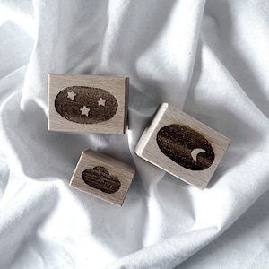 May include: Three wooden blocks with different designs. The first block has a brown oval with three white stars inside. The second block has a brown oval with a white crescent moon inside. The third block has a brown cloud shape.