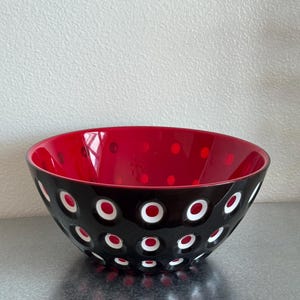 Puede incluir: Un cuenco de cristal redondo con un exterior negro brillante y un patrón de hendiduras circulares. El interior del cuenco es de un rojo vibrante, y las hendiduras circulares del exterior revelan un diseño en capas de color blanco y rojo.