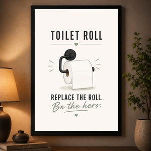 May include: A framed wall art print featuring a black and white illustration of a toilet paper roll on a holder. The text reads TOILET ROLL, REPLACE THE ROLL, and Be the hero, accented with small heart symbols and decorative lines on a white background.