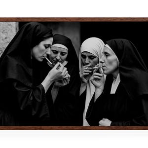 May include: A black and white framed photograph depicting four nuns smoking cigarettes. The nuns are dressed in traditional habits, with some wearing black veils and others white. The image is a close-up, focusing on the nuns' faces and the cigarettes.