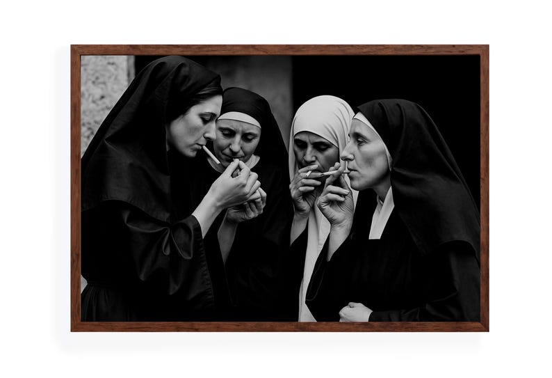May include: A black and white framed photograph depicting four nuns smoking cigarettes. The nuns are dressed in traditional habits, with some wearing black veils and others white. The image is a close-up, focusing on the nuns' faces and the cigarettes.