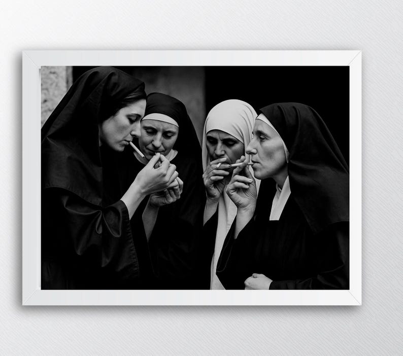 May include: A black and white photograph featuring four nuns in traditional habits, smoking cigarettes. The image is framed in a white border, with the nuns' faces and hands in focus. The nuns are in a close group, with the smoke visible.