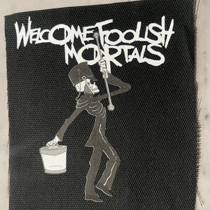 May include: Black and white embroidered patch with a skeleton figure holding a bucket and a stick. The text "Welcome Foolish Mortals" is written in white on a black background.