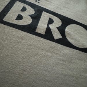 May include: A white t-shirt with black text that reads "THE BRO".