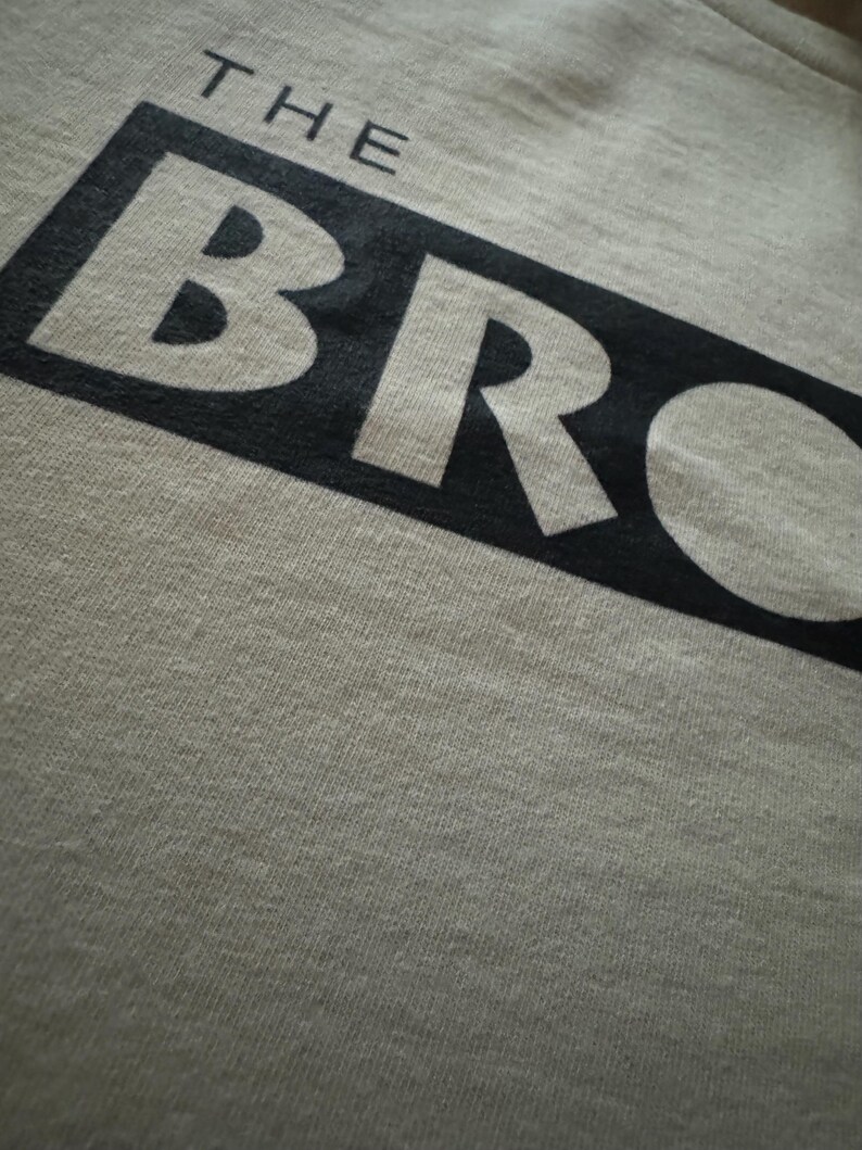 May include: A white t-shirt with black text that reads "THE BRO".