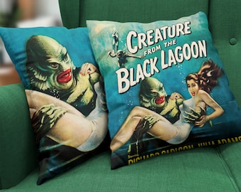 May include: Two blue throw pillows with a vintage illustration of the Creature from the Black Lagoon. The pillow on the right has the movie title and the names of the actors, "Creature from the Black Lagoon", "Starring Richard Carlson, Julie Adams".
