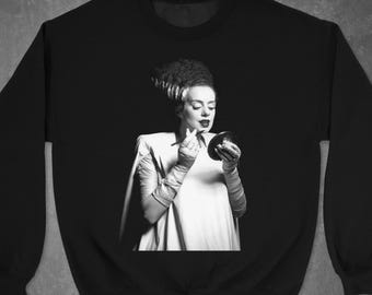 May include: Black and white image of a woman with green hair applying lipstick in front of a mirror. She is wearing a white dress and has a serious expression on her face.