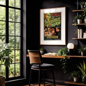 May include: A framed movie poster for The Invisible Man by H.G. Wells, featuring a green-tinted figure and three actors. The poster is displayed on a dark wall above a wooden desk with a chair, a lamp, and several potted green plants.