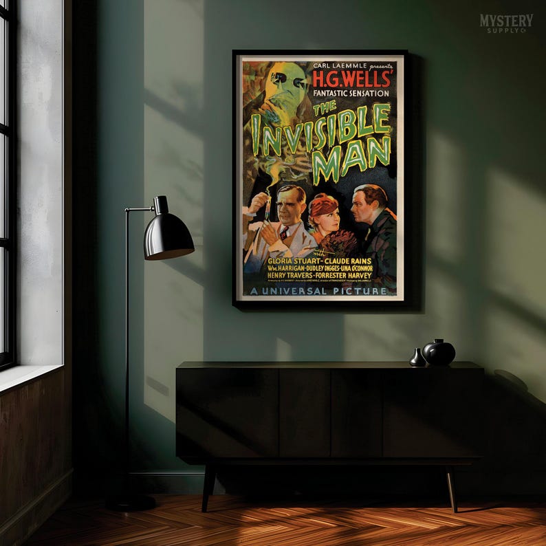 May include: A framed vintage movie poster for The Invisible Man, featuring a central illustration of a man with a bandaged face and goggles, surrounded by three actors, with bold green text and black background details in a rectangular wall display.